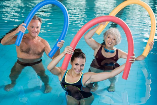 Aqua aerobics with seniors Portrait of smiling people doing aqua fitness together in a swimming pool. Group of senior woman and mature man with swim noodles exercising in a swimming pool. Young trainer and senior people in aqua gym fitness class.